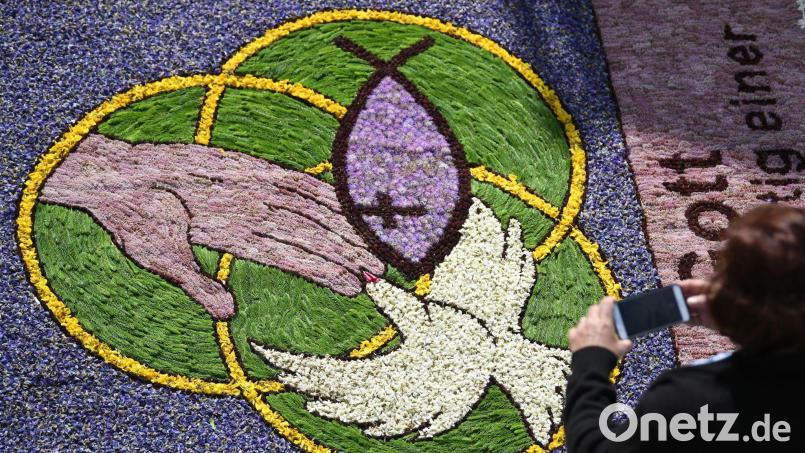 Eine Frau fotografiert an Fronleichnam während der Prozession Kirchenmotive in einem Blumenteppich. Bild: Patrick Seeger/dpa
