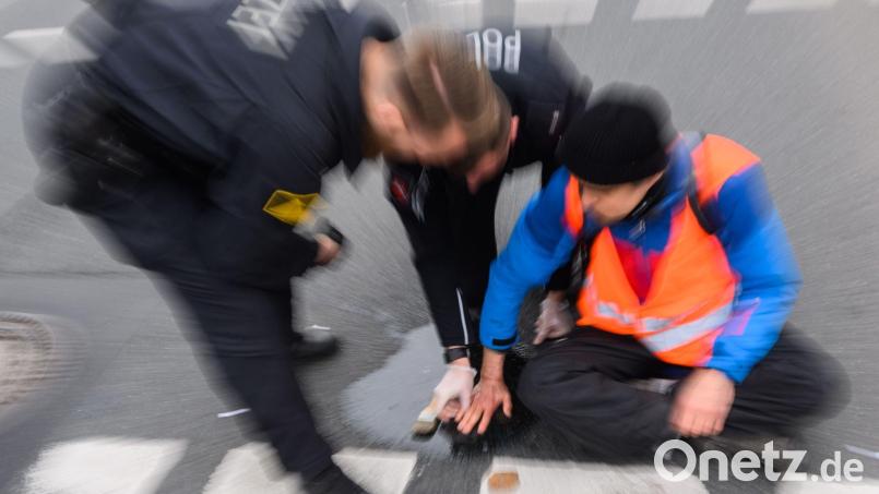 Polizisten versuchen festgeklebte Hände von Aktivisten von der Straße abzulösen. Bild: Julian Stratenschulte/dpa