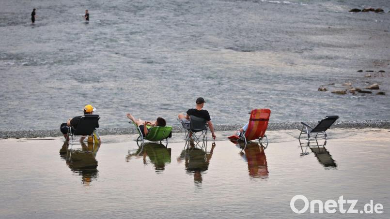 Junge Männer sitzen auf Campingstühlen im seichten Wasser oberhalb des Lechwehrs. Bild: Karl-Josef Hildenbrand/dpa
