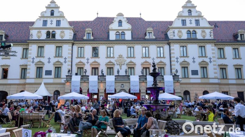 Besucher der Schlossfestspiele sitzen im Garten vor dem Fürstenschloss St. Emmeram. Bild: Armin Weigel/dpa