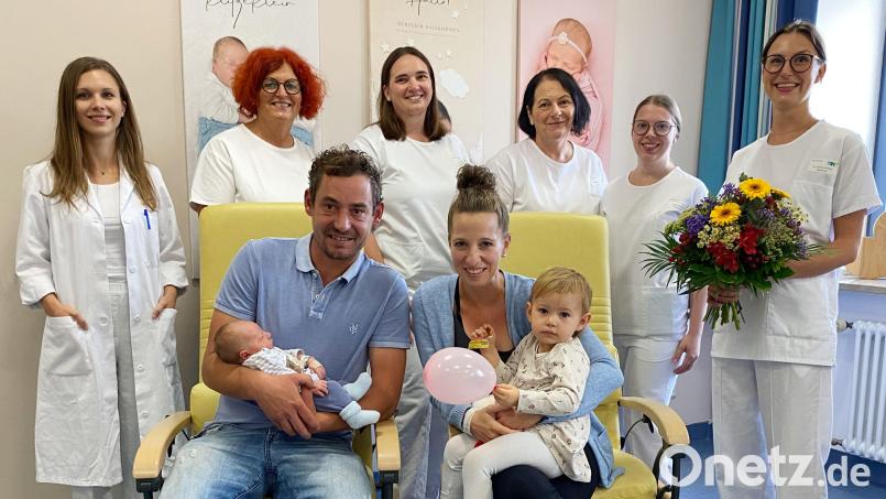 Papa Flo hält den kleinen Max, Schwester Leni nimmt auf dem Schoss von Mama Nicole Platz als MUDr. Denisa Jungwirth, die Hebammen Ruth Mahal-Vollmayr und Julia Witt, Stationsleitung Elisabeth Luksch und ihre Stellvertreterin Anja Zeitlmann sowie Oberärztin Dr. Sophie Schultis (hinten, von links) der Familie gratulieren. Bild: Kliniken Nordoberpfalz, Michael Reindl