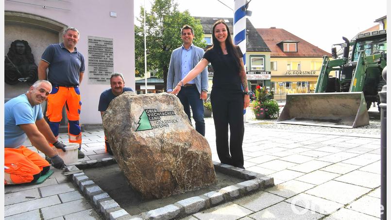 Das Bauhof-Team setzt den Goldnugget zwischen Doktor-Eisenbarth-Brunnen und Maibaum am Marktplatz Oberviechtach ab. Bürgermeister Rudolf Teplitzky und Margit Boch vom Stadtmarketing hoffen auf ein beliebtes Fotomotiv: Der Gneis-Findling erhält noch eine Goldfarbe. Bild: Portner
