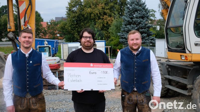 Im feschen Vereins-Outfit überreichen Vereinsvorsitzender Sebastian Wohlrab und Kassenverwalter Siegfried Zimmermann auf der Baustelle den symbolischen Spendenscheck an Pfarrer Johannes Bosco. Bild: do