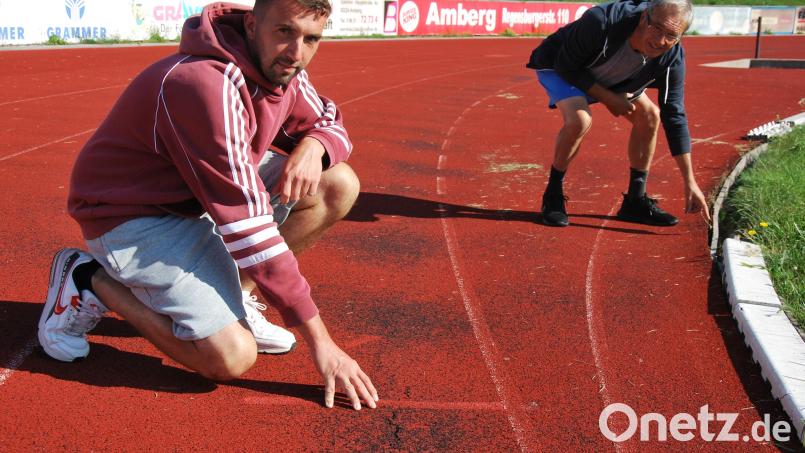 Christoph Schuster (ESV Amberg, links) und Andrea Bellotto (TV Amberg, rechts) zeigen die Schäden der Lauffläche der 400-Meter-Bahn. Bild: gsp
