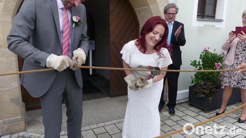 Während sich Thomas Ott mit einem Taschenmesser abmüht, schreitet seine Frau Romana mit einem Bolzenschneider zur Tat. Bürgermeister Bernhard Stangl applaudiert. Bild: rn