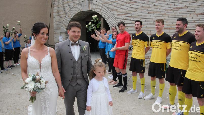 Laura und Fabian Büttner passieren mit Patenkind und Brautmädchen Greta das Ehrenspalier, bestehend aus Spielern des FC Tirschenreuth und Arbeitskolleginnen der Braut (hinten). Bild: kro