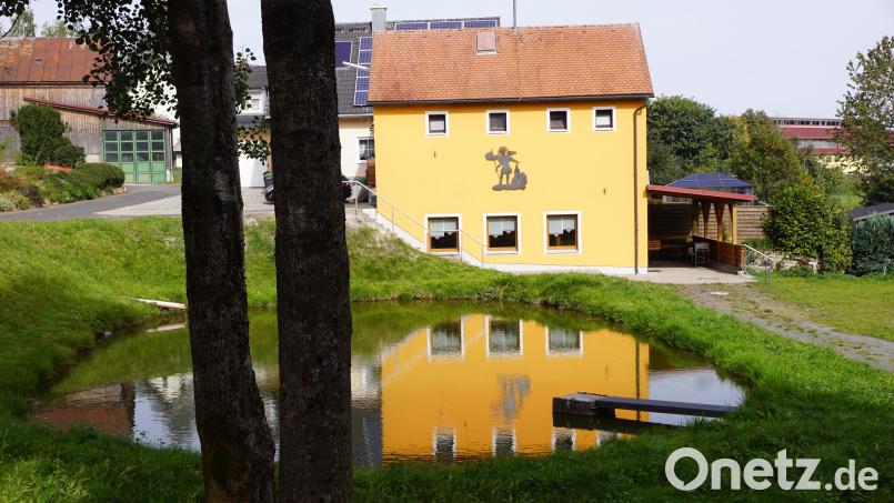 Auf der Wasseroberfläche des Teiches, der nun offiziell ein Dorfteich ist, ist die Spiegelung des dahinterliegenden Feuerwehrgerätehauses zu sehen. Bild: bkr