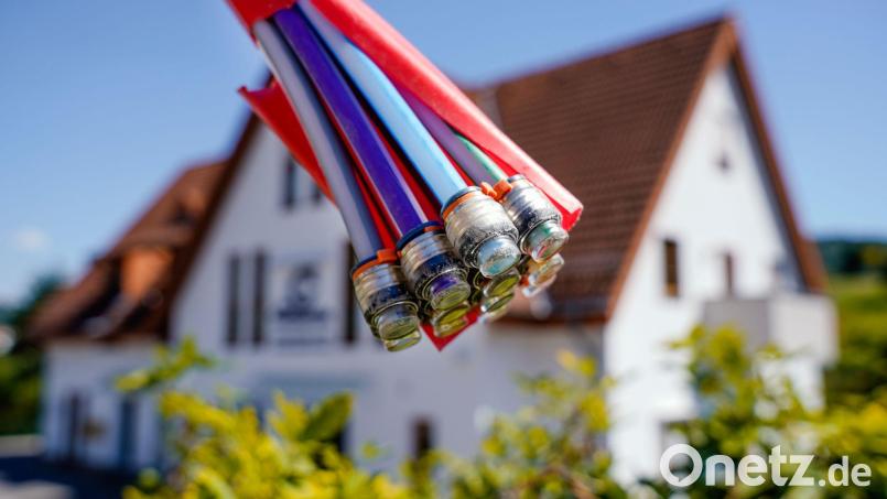 Ein Bündel mit Umhüllungen für Glasfaserkabel hängt vor einem Wohnhaus. Symbolbild: Uwe Anspach/dpa