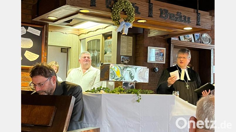 Gerd Hennecke am Harmonium (links), hinter dem Tresen Wirt Armin Ertel und Dekan Karlhermann Schötz. Der Tresen war mit einem weißen Tuch zum Altar gemacht und mit Hopfenkränzen für den Gottesdienst verziert worden. Bild: Max Klose/exb