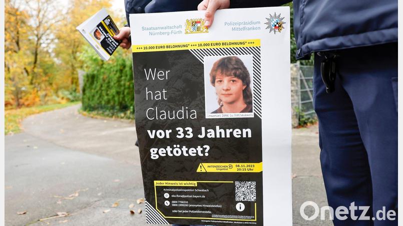 Ein Polizist mit einem Plakat zum Mordfall von 1990 in Röthenbach an der Pegnitz. Bild: Daniel Löb/dpa
