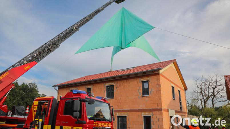 Die Drehleiter der Feuerwehr Hirschau hievt das hellgrüne Folien-Notdach über den Neubau, der als Übungsobjekt dient. Bild: Wolfgang Steinbacher
