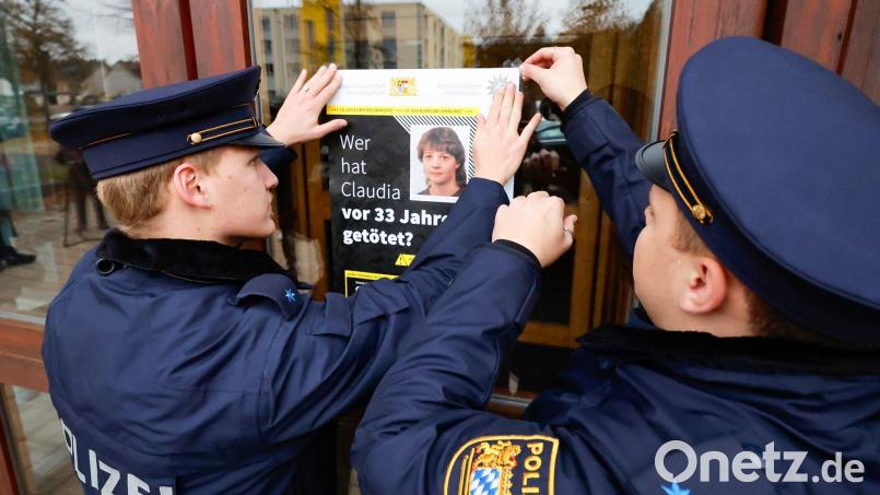 Polizisten hängen das Plakat zum Cold-Case von Claudia Obermeier an einer Glasscheibe auf. Bild: Daniel Löb/dpa