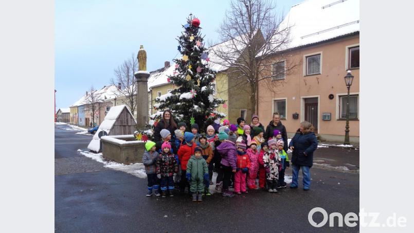 Stolz präsentieren sich die Kinder mit ihren Betreuerinnen und der Familienbeauftragten Andrea Kunschir vor dem geschmückten Baum. Neben der Mariensäule steht der Krippenstall. Bild: Mösbauer/exb