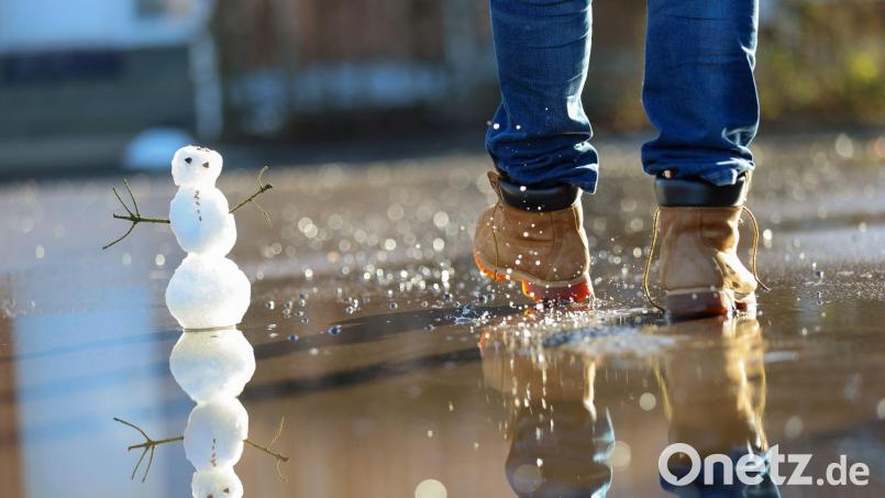 Ein Mann läuft durch eine Pfütze mit Tauwasser, in der ein Schneemann steht. Bild: Thomas Warnack/dpa/Symbolbild
