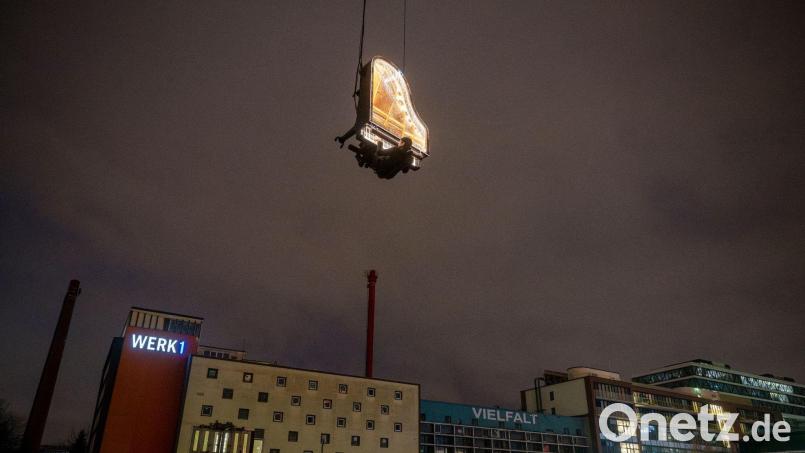 Der Künstler Alain Roche sitzt an seinem beleuchteten Flügel, der an einem Kran gehalten wird. Bild: Peter Kneffel/dpa