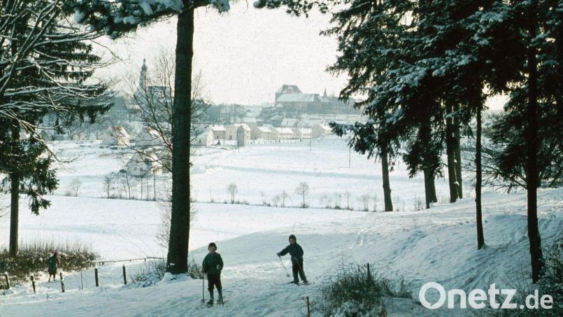 Zwei Kinder auf Skiern in einer Winterlandschaft vor prächtiger Sulzbach-Rosenberger Stadtkulisse: Ende der 1950er, Anfang der 1960er Jahre war Wintersport auch im Bereich des heutigen Stadtteils Erlheim öfters möglich. Bild: Archiv Ostermann