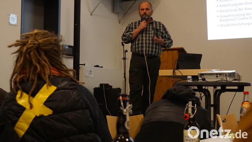 Der vom geplanten Süd-Ost-Link betroffene Störnsteiner Landwirt Helmut Meiler spricht auf der Bühne über seine Befürchtungen, wenn bald die Bagger anrücken sollten. Im Publikum hört eine Frau zu, die ein gelbes Kreuz als Zeichen des Protests auf ihre Jacke geklebt hat. Bild: jut