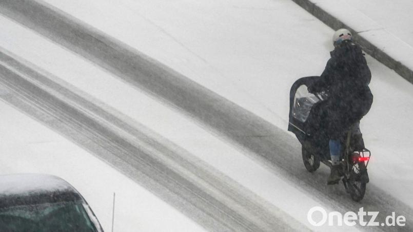 Eine Frau fährt mit einem Lastenfahrrad in Hamburg über eine verschneite Straße. Bild: Marcus Brandt/dpa
