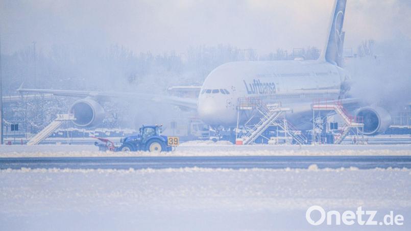 Ein Schneeräumer fährt im Schneetreiben auf dem Flughafen vor einer Maschine entlang. Bild: Jason Tschepljakow/dpa
