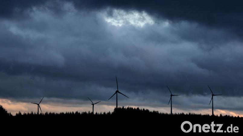 Windräder stehen unter dichten Regenwolken hinter einem Wald. Bild: Karl-Josef Hildenbrand/dpa