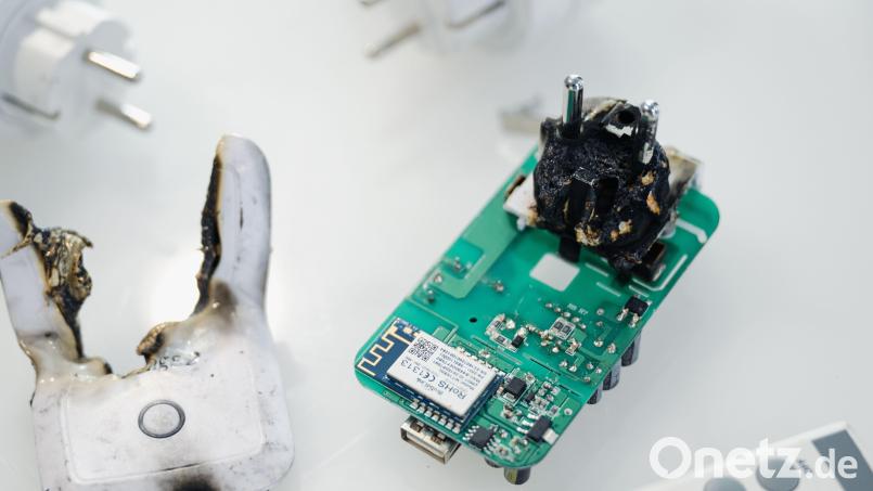 Eine verbrannte Funksteckdose liegt in einem Schaukasten. Hätte man einen technischen Defekt frühzeitig erkennen können? Symbolbild: Marius Becker /dpa