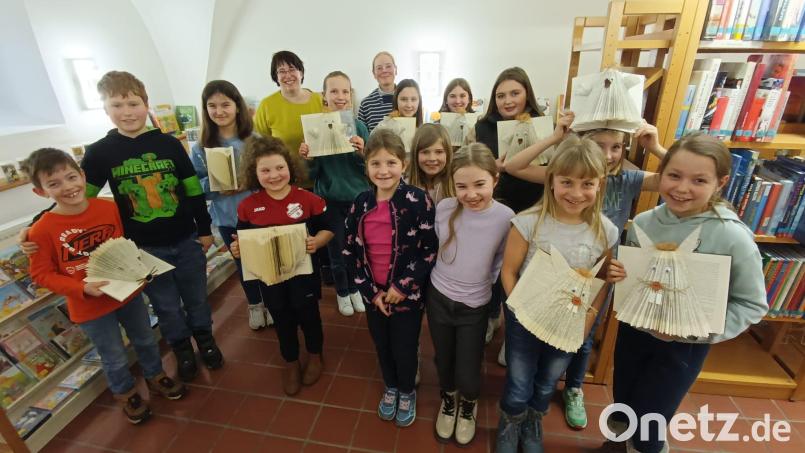Stolz zeigen die Kinder die Ergebnisse des Buchfalt-Workshops. Hinten Büchereileiterin Maria Klobes-Martin (rechts) und die Expertin Christine Simmel (links). Bild: wku