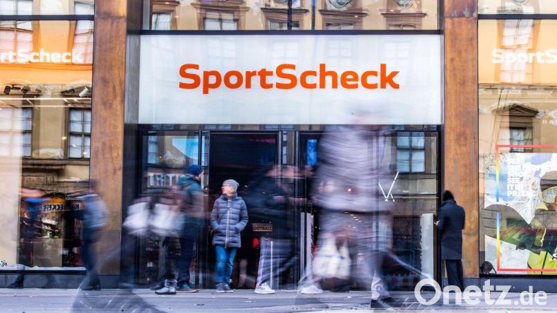 Personen gehen an einer Sportscheck-Filiale in der Münchener Fußgängerzone vorbei. Bild: Lino Mirgeler/dpa