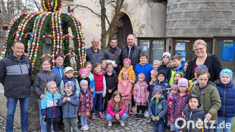 Mit Liedbeiträgen zum Osterfest erfreuen die Kinder mit Leiterin Susanne Hausmann (rechts) vor dem Osterbrunnen alle Anwesenden. Bild: knh