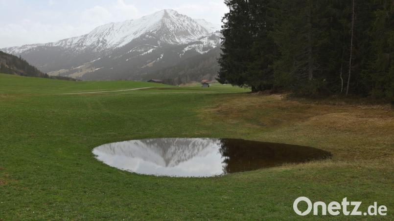 Die im Dunst liegenden Alpen spiegeln sich in einem Weiher. Der Saharastaub-Höhepunkt ist überschritten. Bild: Karl-Josef Hildenbrand/dpa