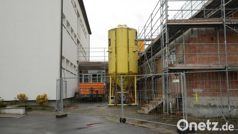 Zwischen der Schule (links) und der Mehrzweckhalle (rechts) muss das Stahlrohr für die Aufnahme von Kanal und Wasserleitung verlegt werden. Es ist ein echter neuralgischer Punkt, weil das Stahlrohr tiefer gelegt werden muss als die Fundamente der beiden Gebäude in den Boden verbaut sind. Außerdem ist das Grundwasser ein nicht zu übersehendes Problem. Bild: bey