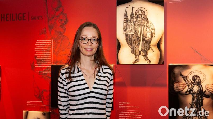 Die Museumsleiterin und Kuratorin Christine Demele steht vor einer Ausstellungstafel mit Fotografien von Tätowierungen, die nach Kunstwerken von Albrecht Dürer entstanden sind. Bild: Oliver Frank/Albrecht-Dürer-Haus/dpa