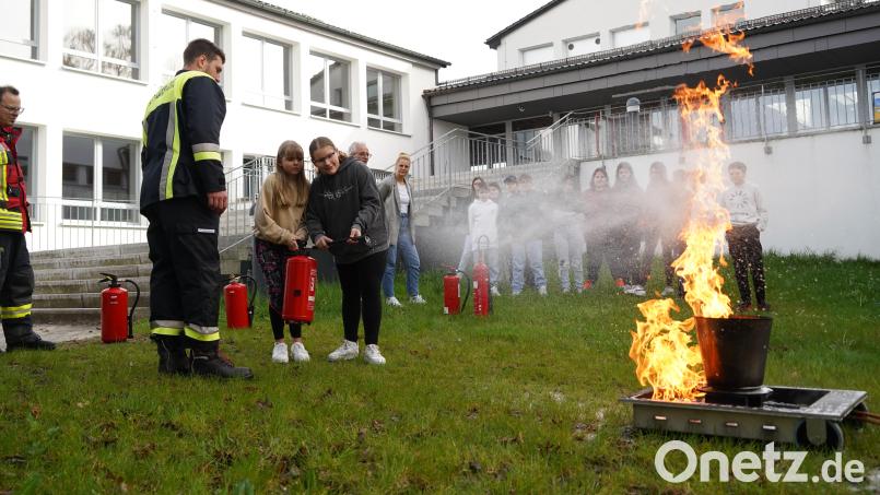 30 Feuerwehrleute aus 13 Feuerwehren präsentieren sich und ihr Ehrenamt beim Feuerwehrtag an der Mittelschule Ebnath. Edyta Kaczmarczyk und Katharina Heimerl (von links) probieren einen Feuerlöscher aus. Infos gibt Julian Heinl, Kommandant bei der Feuerwehr Schwarzenreuth. Bild: kaz