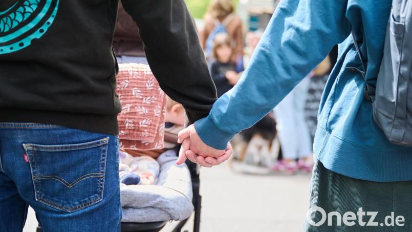 Eltern halten Händchen, während sie mit ihrem Baby im Kinderwagen über einen Markt gehen. Symbolbild: Annette Riedl/dpa