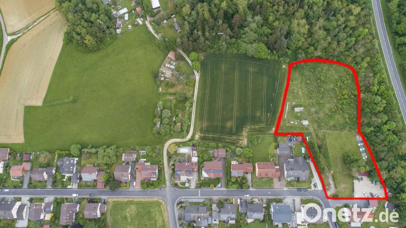 Die Streuobstwiese (Bildmitte) nördlich der Bebauung teilt das geplante Neubaugebiet in eine rechte und linke Hälfte. Ginge es nach den Anliegern der Sauerzapfstraße, soll die rechte Hälfte (dunkelgrün) nur über die Sauerzapfstraße (Schotterweg und Straße rechts unten) erschlossen werden. Genau auf dieser Zufahrt befürchtet die Stadt Probleme mit Altlasten durch eine frühere Maxhütten-Deponie (rote Umrandung). Teile der Flächen gehören dort dem Freistaat. Bild: Thilo Hierstetter