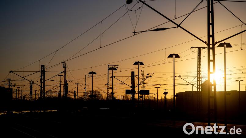 Die Sonne geht hinter Oberleitungen an einem Bahnhof unter. Bis die Strecken in Nordostbayern elektrifiziert sind, wird es noch lange dauern. Die Trassen für die Bahnstromleitungen, die die Energie an die Gleise bringen sollen, sind noch nicht festgelegt. Bild: Hauke-Christian Dittrich/dpa