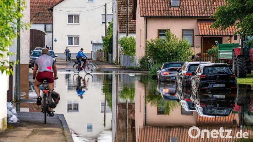 Radler fahren durch eine überflutete Straße. Bild: Armin Weigel/dpa