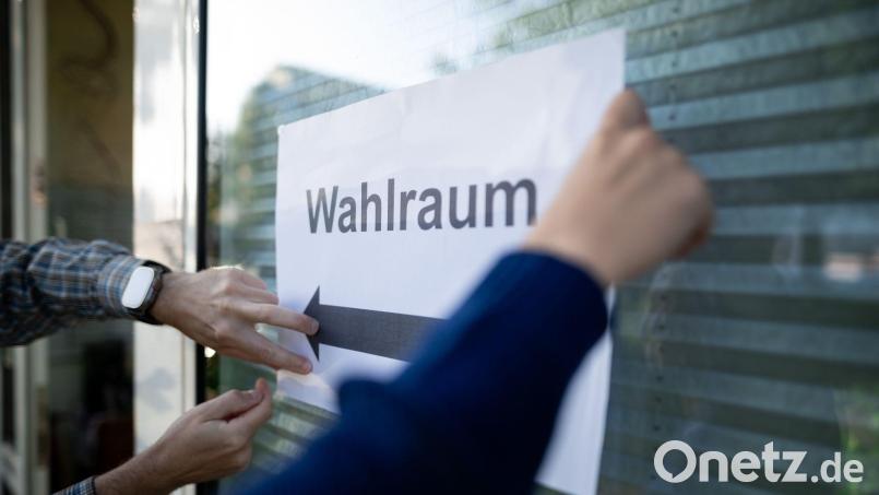 Wahlhelfer hängen einen Zettel, auf dem „Wahlraum“ steht, auf. Bild: Fabian Strauch/dpa