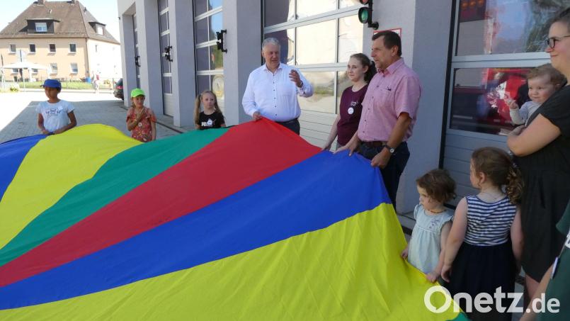 Kinder und Ehrengäste breiten das große bunte Tuch aus dem Fundus von Spielebus Maxl aus. Bild: ge