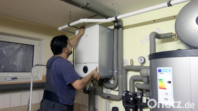 Ein Handwerker befestigt die Abdeckung an einer Steuereinheit einer Wärmepumpe im Keller eines Wohnhaues. Mit der Energiewende verändert sich auch der Beruf des Heizungsbauers. Symbolbild: Doreen Garud/dpa