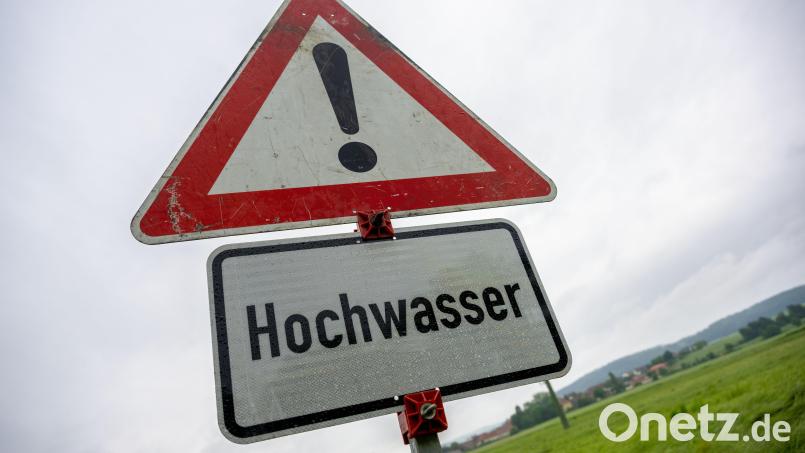 Regentropfen hängen an einem Schild, das vor Hochwasser warnt, Wolken am Himmel verheißen weiteren Niederschlag. Im Landkreis Schwandorf ist die Lage ruhig. Symbolbild: Pia Bayer /dpa