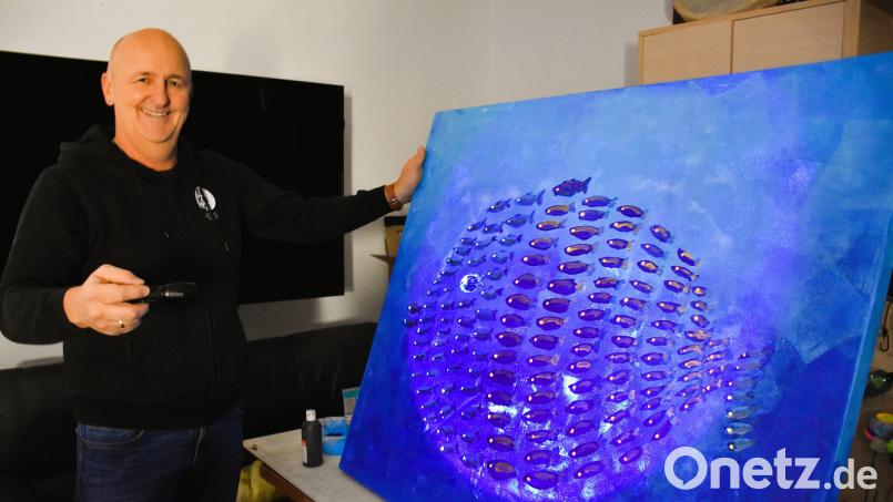 Jürgen Frischholz zeigt als Beispiel eines der fluoreszierenden Gemälde, das er selbst gemalt hat. Das Bild gibt es auch bei der Ausstellung zu sehen. Bei entsprechend richtiger Leuchttechnik wird der Effekt natürlich weit eindrucksvoller herausgearbeitet sein. Bild: ubb