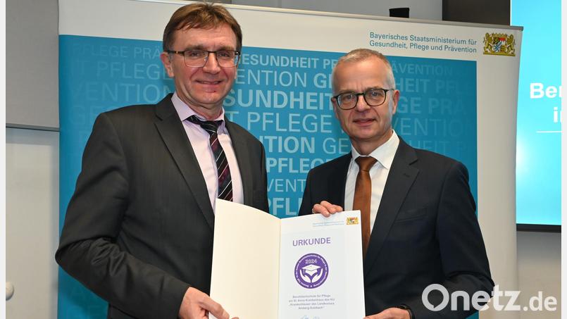 Schulleiter Hans-Jürgen Bruhn (links) freut sich über die Urkunde, die ihm Dr. Rainer Hutka (rechts), Amtschef des Staatsministeriums für Gesundheit und Pflege, überreichte. Bild: Staatsministerium für Gesundheit und Pflege/exb