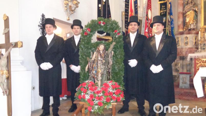 Vier junge Männer mit Frack und Zylinder tragen die geschmückte Statue. Archivbild: amö