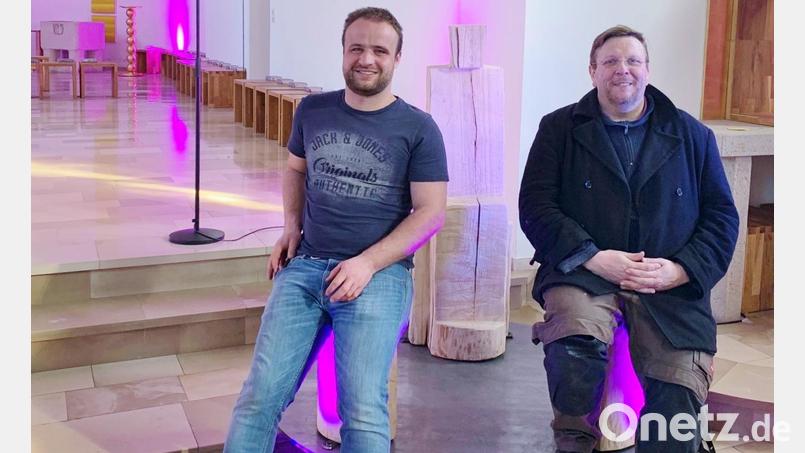 Pfarrer Markus Meier (rechts), Holzbildhauer Marco Bruckner und das dreiteilige Kunstwerk &quot;Einfach da sein&quot;, auf dem man auch sitzen kann, wie zu sehen ist. Bild: Tobias Wagner/exb