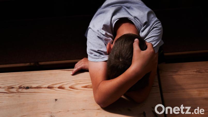 Ein Kind versteckt sein Gesicht unter seinen Armen und liegt mit dem Kopf auf einem Tisch. Körperliche und emotionale Misshandlungen von Kindern können weitreichende Folgen haben. Symbolbild: Annette Riedl/dpa