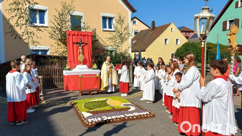 Pfarrer Alfons Kaufmann trägt am ersten Altar das Evangelium vor. „Mit Jesus im Boot“ lautet der Spruch im kunstvollen Blumenteppich der Kolpingfamilie. Bild: lg