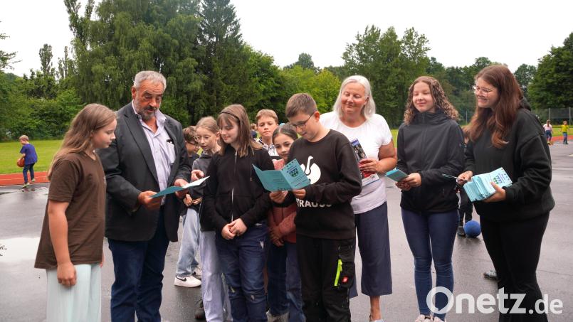 Bürgermeister Josef Beimler übergibt auf dem Pausenhof der Wolfgang-Caspar-Printz Grundschule das von Marina Daubenmerkl (rechts) und Praktikantin Julia Herold (Zweite von rechts) von der Marktverwaltung zusammengestellte diesjährige Waldthurner Kinderferienprogramm. Bild: fvo