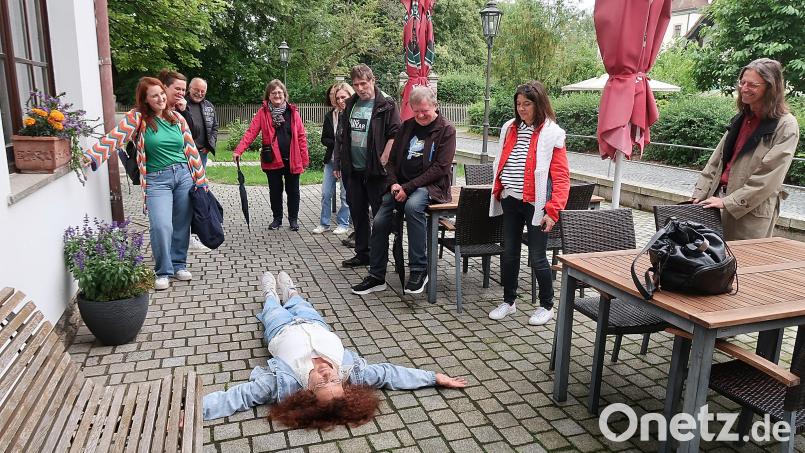 Zur Freude der Teilnehmer wurden bei der Drehort-Tour durch Friedenfels auch Szenen nachgespielt, wie hier von Ulla Britta Baumer (auf dem Boden liegend) die Szenerie, als sie im Film mausetot vor der Eingangstür des Friedenfelser Dorfladens liegen musste. Bild: bsc