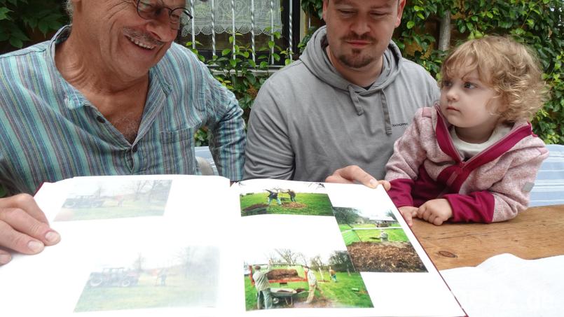Der Störnsteiner Schnapsbrenner Wolfgang Kriechenbauer schaut sich mit Sohn Hannes und Enkelin Neele im Fotoalbum die Bilder von der Pflanzaktion für die neue Streuobstwiese an. Bild: Uwe Ibl