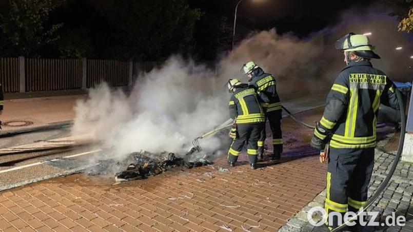 Die zur Abholung bereitgestellten Papiercontainer an der Pfalzgraf-Friedrich-Mittelschule brennen vollständig ab. Auch der Asphalt des Gehsteigs wird in diesem Bereich in Mitleidenschaft gezogen. Die Feuerwehrkräfte können nur mehr Nachlöscharbeiten durchführen. Bild: Anton Schwägerl/exb
